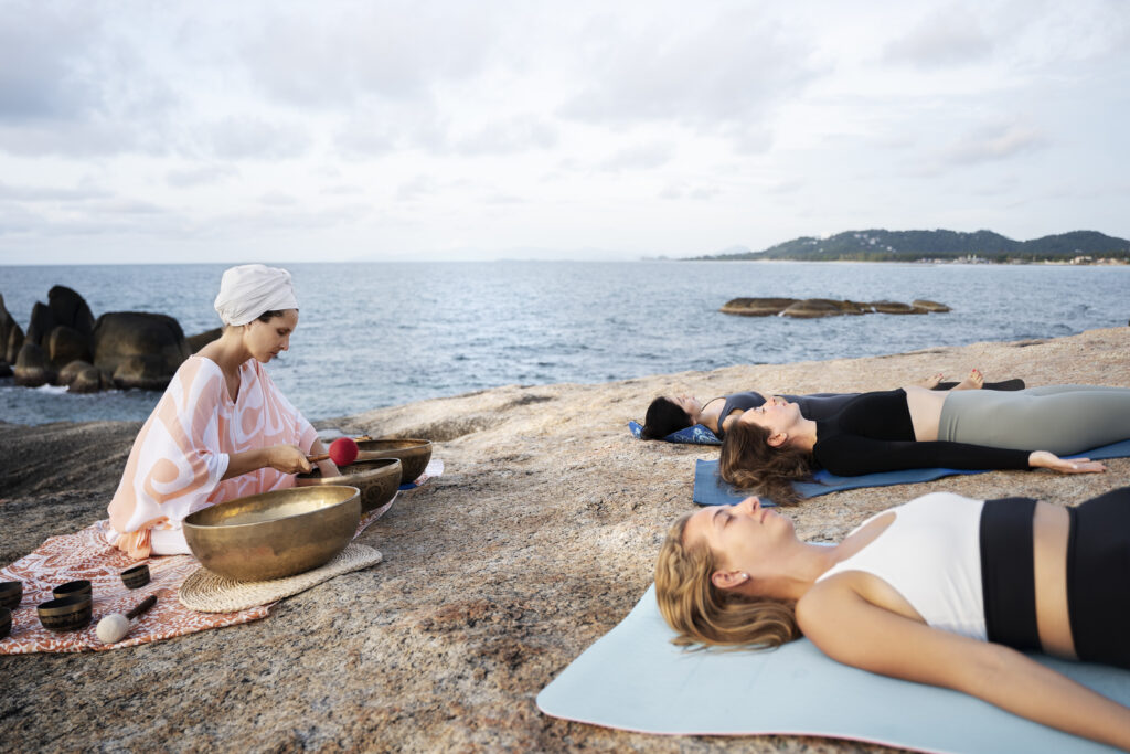 Mulheres participando de retiro de bem-estar com meditação sonora à beira-mar durante viagem transformacional.