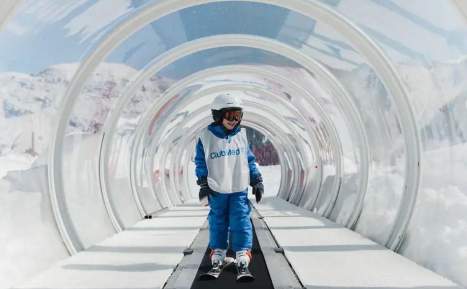 Criança aprendendo ski em área infantil do resort Club Med nos Alpes.