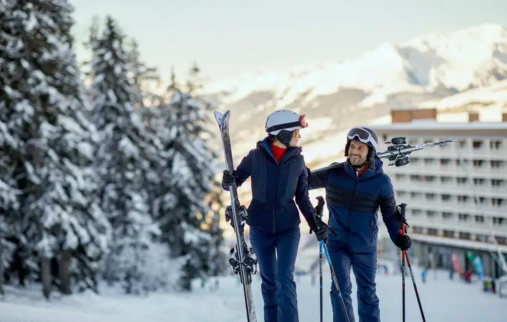 Casal com equipamentos de ski em resort nos Alpes.